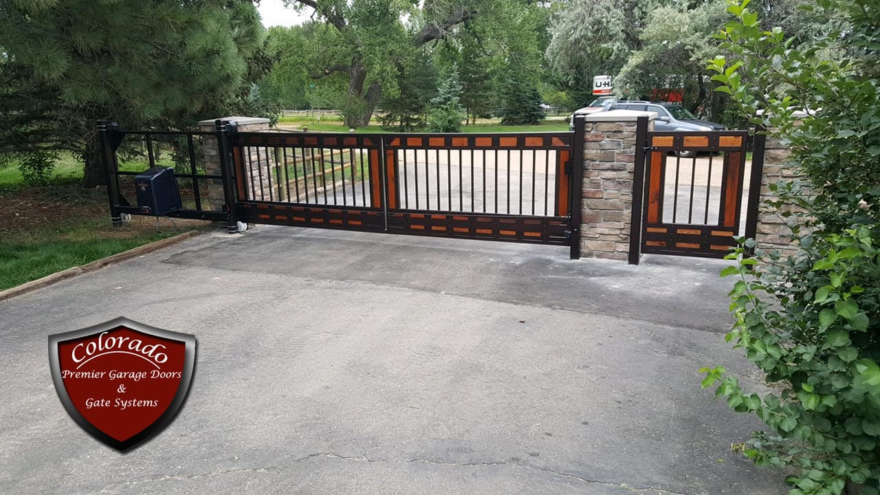Black iron slide gate with cedar inlays and a matching walk gate between stone pillars