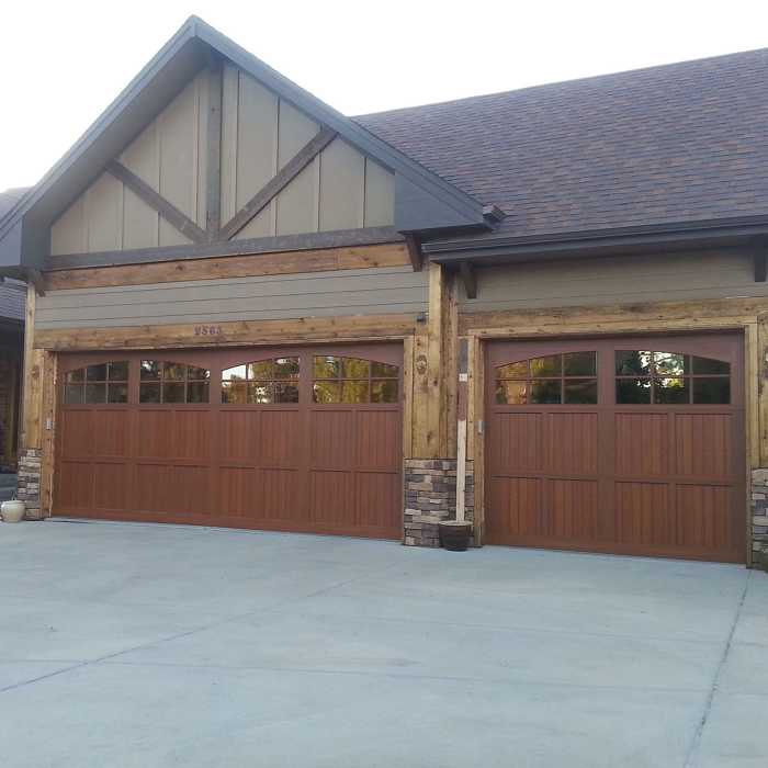 Two stained wood carriage-style garage doors on a timber and stone house