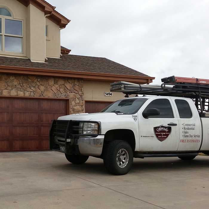 Colorado Premier service truck with ladder rack parked in front of a stained wood garage door